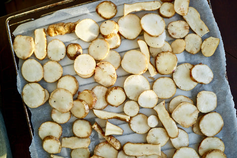 A lined baking tray with slices of potatoes