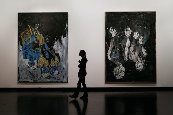 person in an art gallery in front of two large paintings