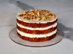 naked carrot cake layered with cream cheese frosting topped with crushed walnuts