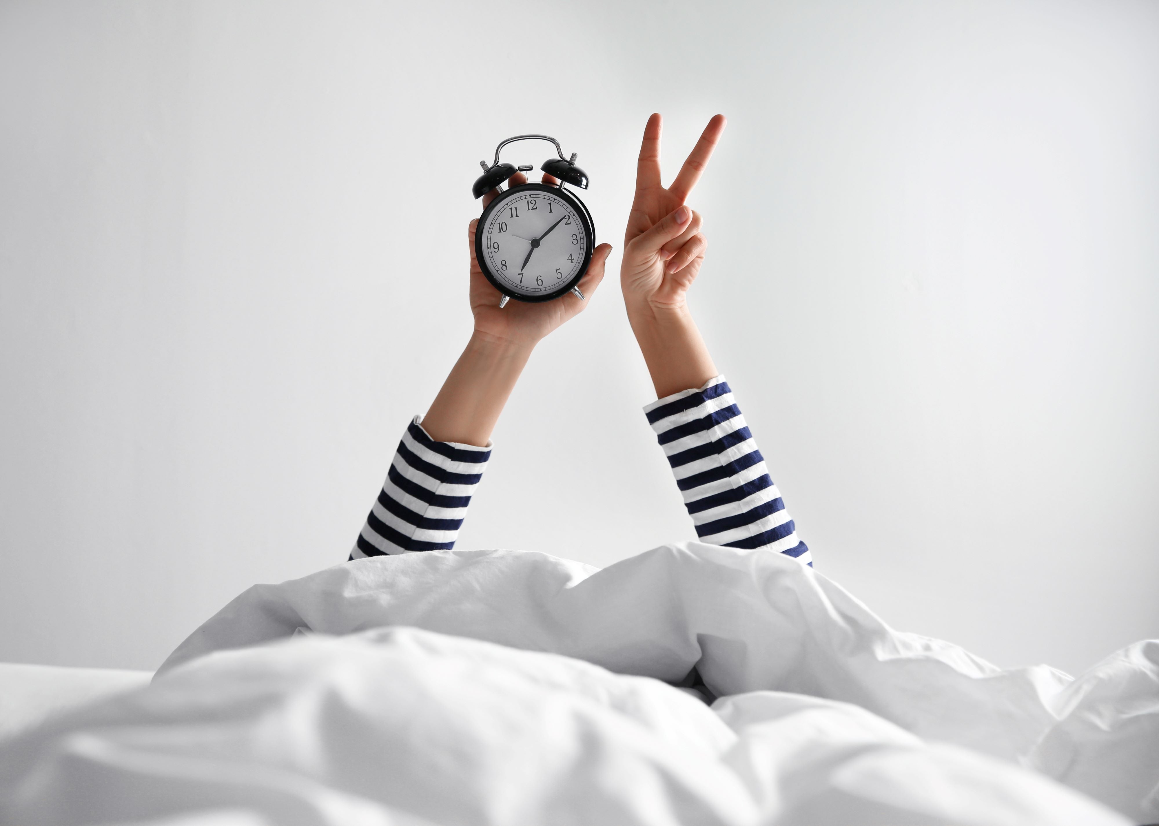 arms of woman holding an alarm clock with one hand and making the sign of love and peace with the other