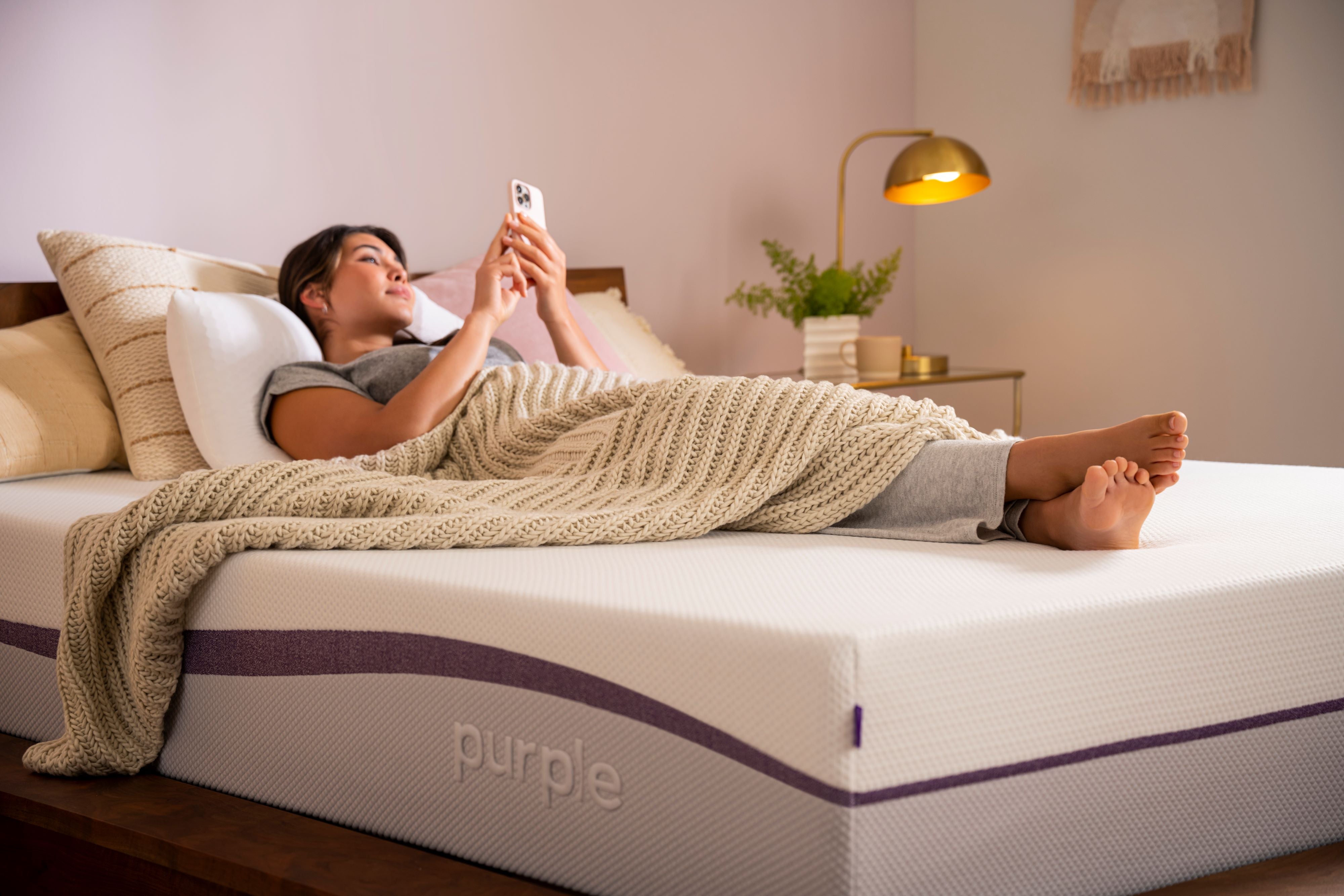 Woman resting on a Purple Plus mattress while checking her phone