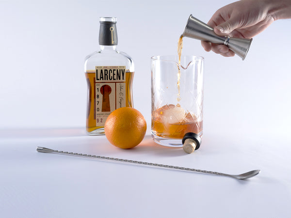 Bourbon being poured out of jigger into mixing glass with other ingredients. 