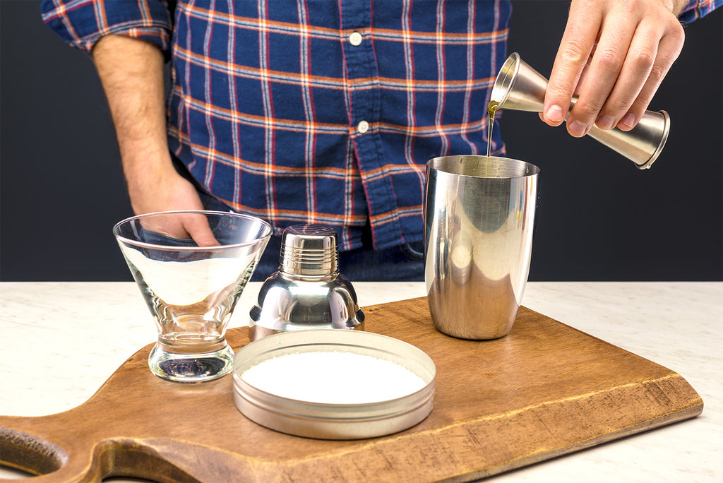 Person pouring simple syrup into a cocktail shaker with a jigger. 