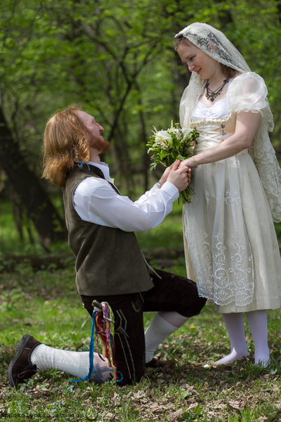 Groom kneeing holding his brides hand. She is wearing an ivory and champange dirndl wedding dress and bridal veil