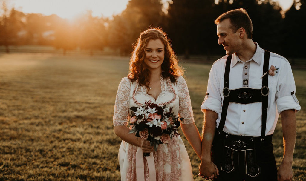 Woman wearing a dirndl wedding dress holding a bouquet of flowers with her husband on their wedding day