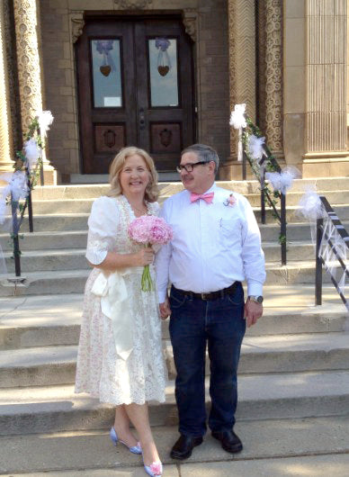 Bride wearing an ivory and prink floral cotton wedding dirndl standing on the church steps with her groom