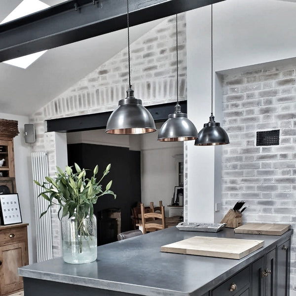 Trio of pewter pendants over a kitchen island with exposed brick walls