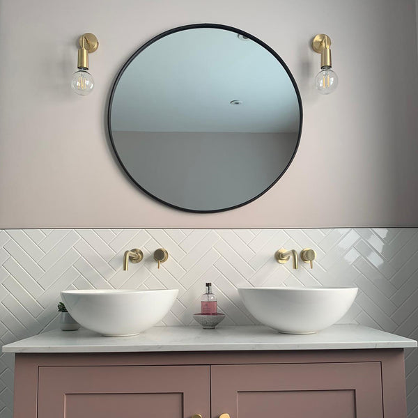 Pink bathroom interior with circular mirror and brass wall lights