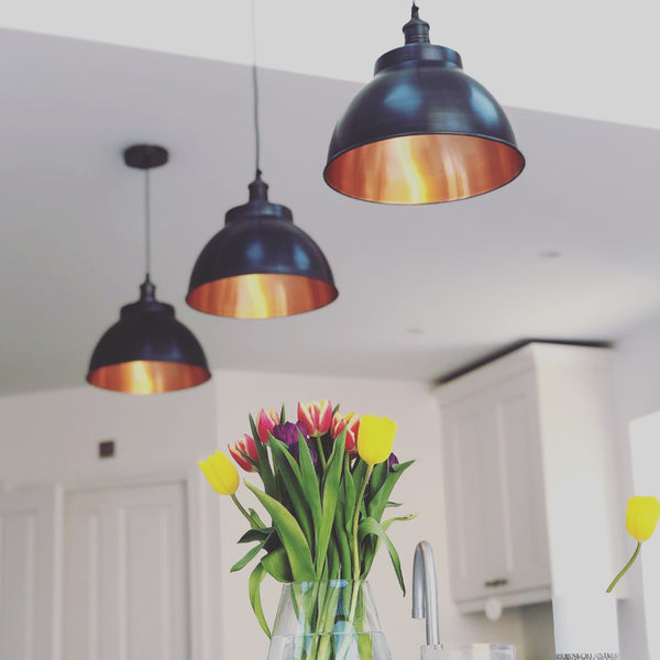 Trio of pewter and copper industrial lights in a kitchen interior with flowers