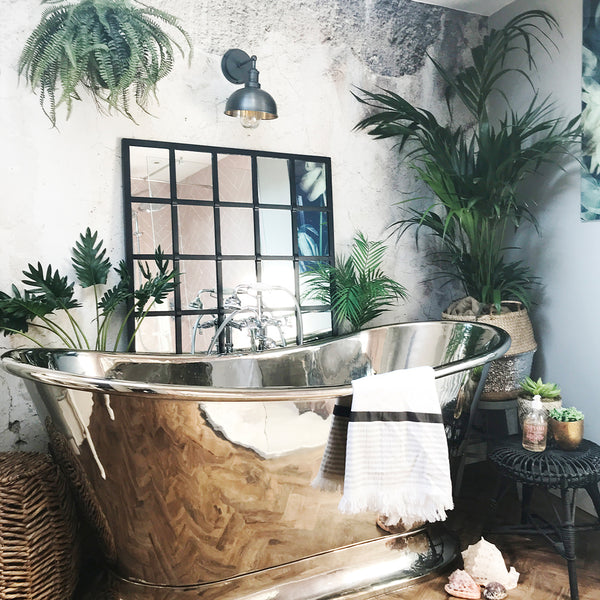 A metallic bathtub and large mirror surrounded by tropical plants