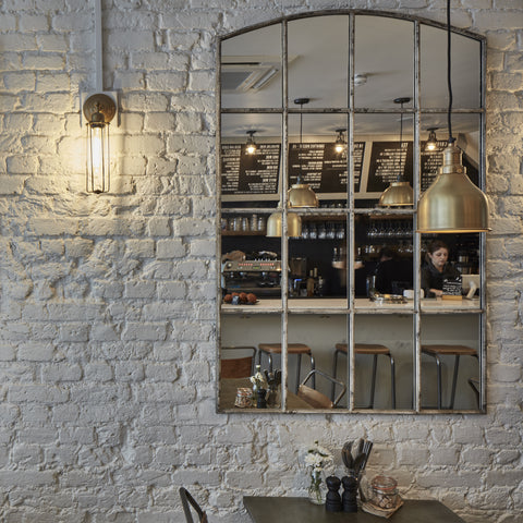 A mirror on a white brick wall with industrial lights by Industville