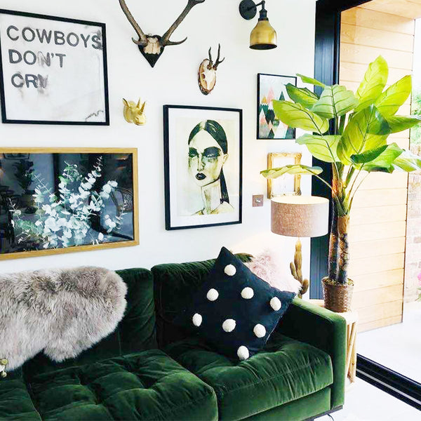 Emerald green velvet sofa in a living room interior with wall art and brass wall light