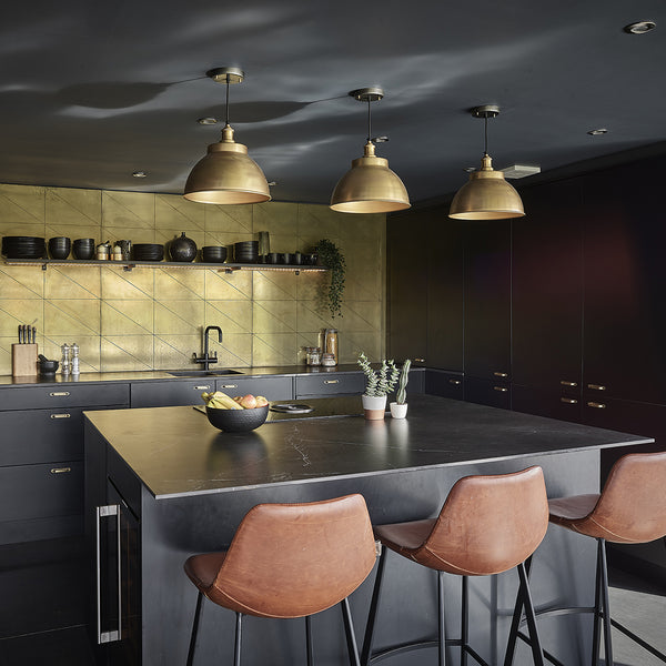 A trio of brass industrial pendant and brass lights over a kitchen island 