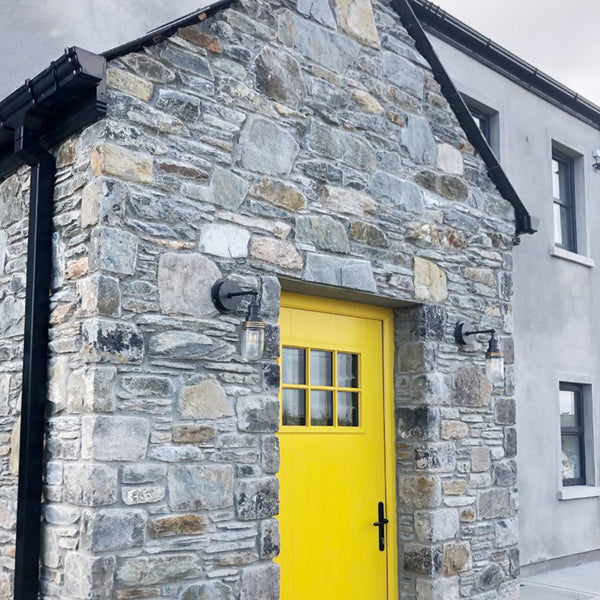 Grey brick building with a yellow front door and pewter industrial outdoor wall lights