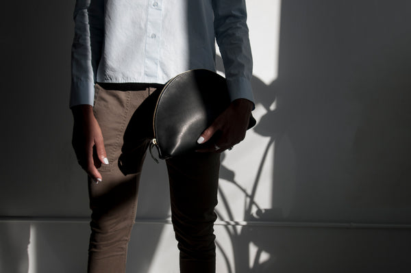 Female model standing in the sunlight holding a leather clutch