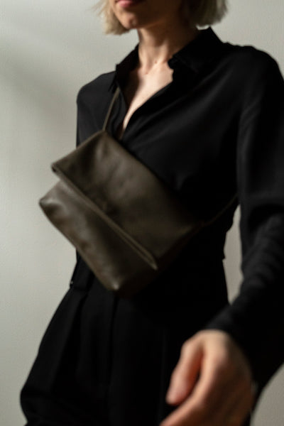 female model walking with a taupe leather crossbody bag