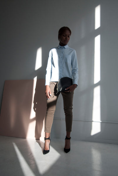 Female model standing in the sunlight holding a leather clutch