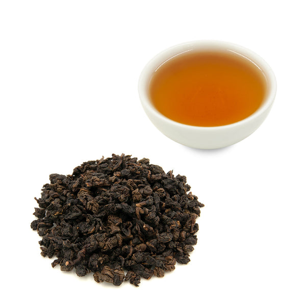 Brewed Tie Guan Yin Oolong Tea in a white tea cup behind a pile of dry tea leaves