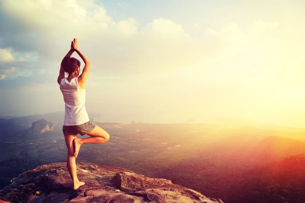 girl doing yoga on top of mountain