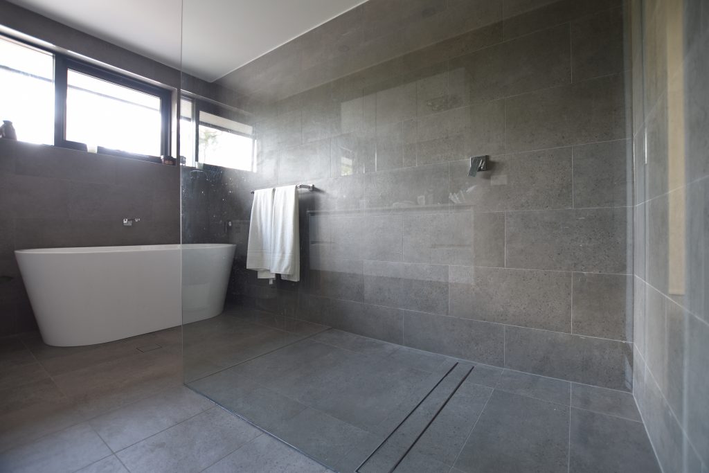 Bathroom with walk in shower and long tile insert grate, this is good for cleaning.