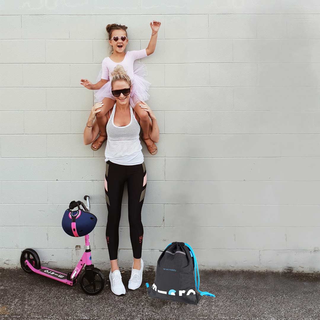 Mum with daughter on her shoulders on the way to school with pink scooter