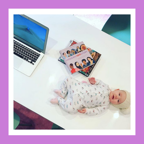 Baby laying on a table next to a laptop and stack of books