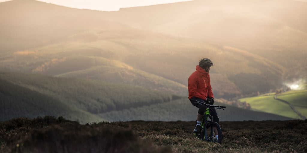 A man sat on his bike on top of a hill and watching the sun set