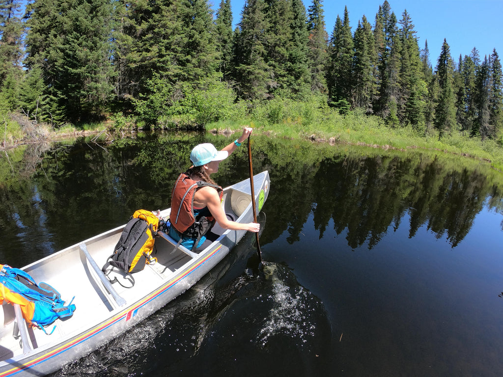 woman paddling canoe on calm lake in summer 