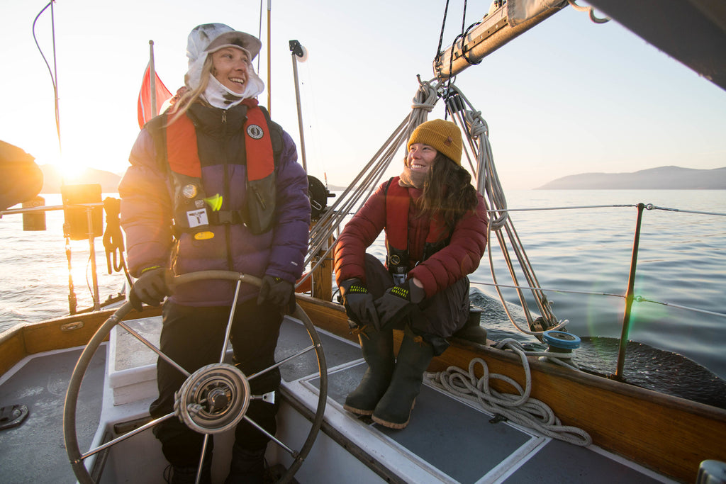 two women navigating a sail boat wearing mustang pfd's