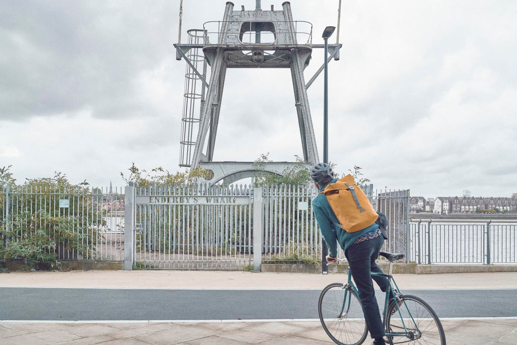 Photographer Joe McGorty cycling the Thames Footpath wearing an orange waterproof Utility Archive backpack