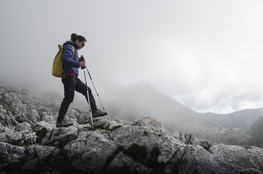 Hiker striding over boulders on cloudy mountainside.