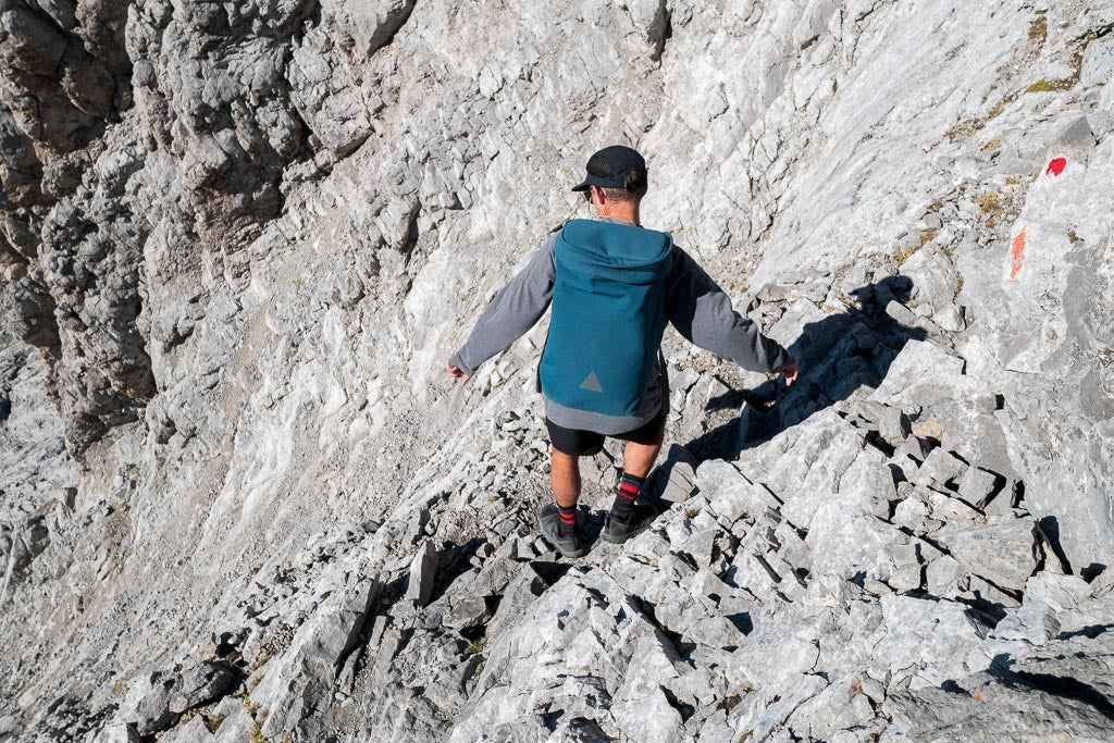 Man with blue backpack hiking down steep rocky path