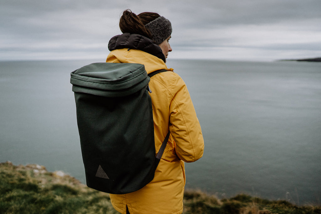 Woman looking out to sea in yellow coat and grey backpack