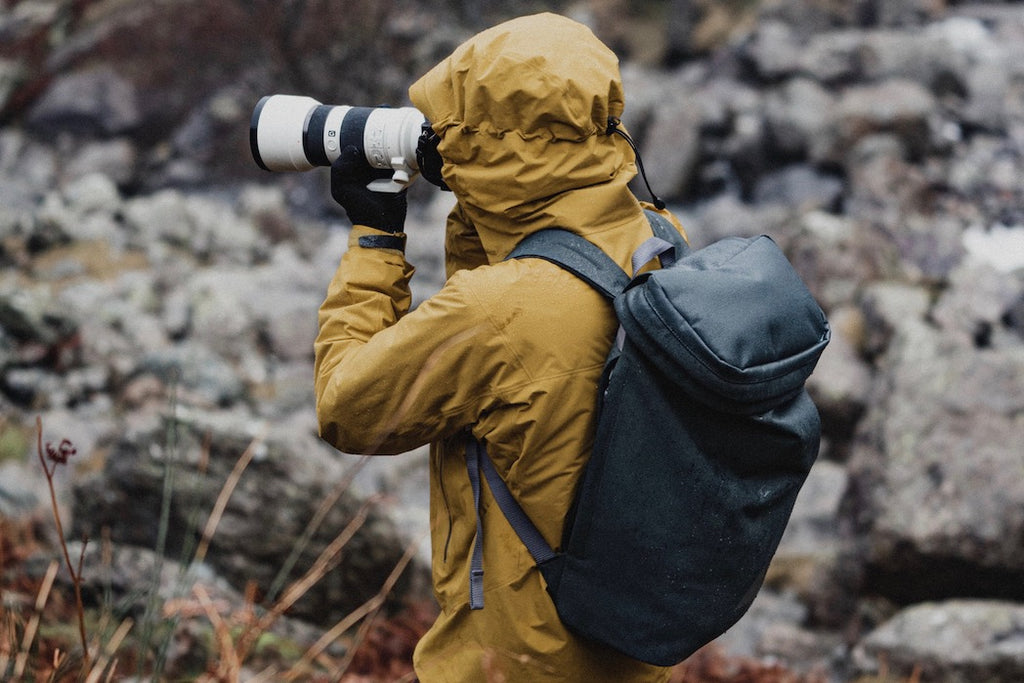 Photographer outdoors on wet day in yellow rain jacket and grey backpack