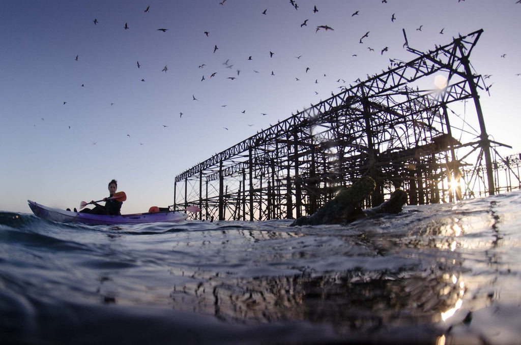 Derelict Brighton West Pier as sun sets on clear day, kayak and seagulls