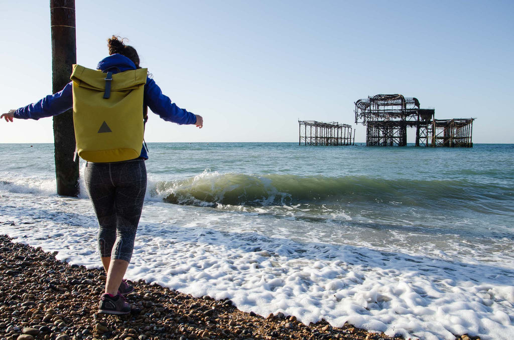 Woman with yellow backpack, skipping in waves, Brighton beach, West Pier in background