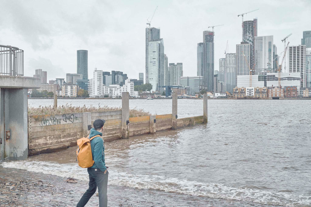 Photographer Joe McGorty wearing an Utility Archive backpack looking across the Thames to the London Docklands skyline
