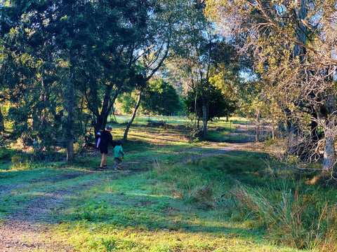 image shows natural bush valley with a path through the middle. woman carrying a baby on one hip and holding another childs hand