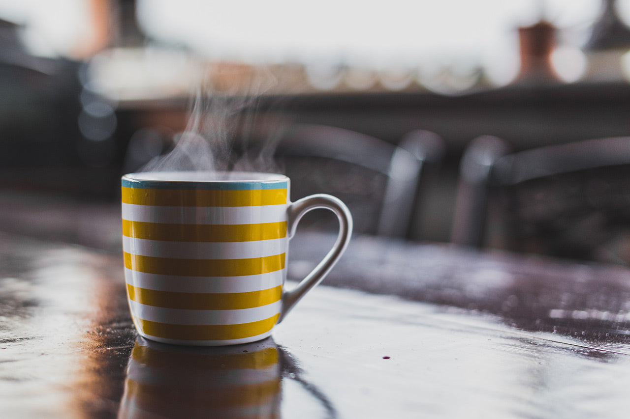 Yellow and white stripy mug with steam on kitchen table.