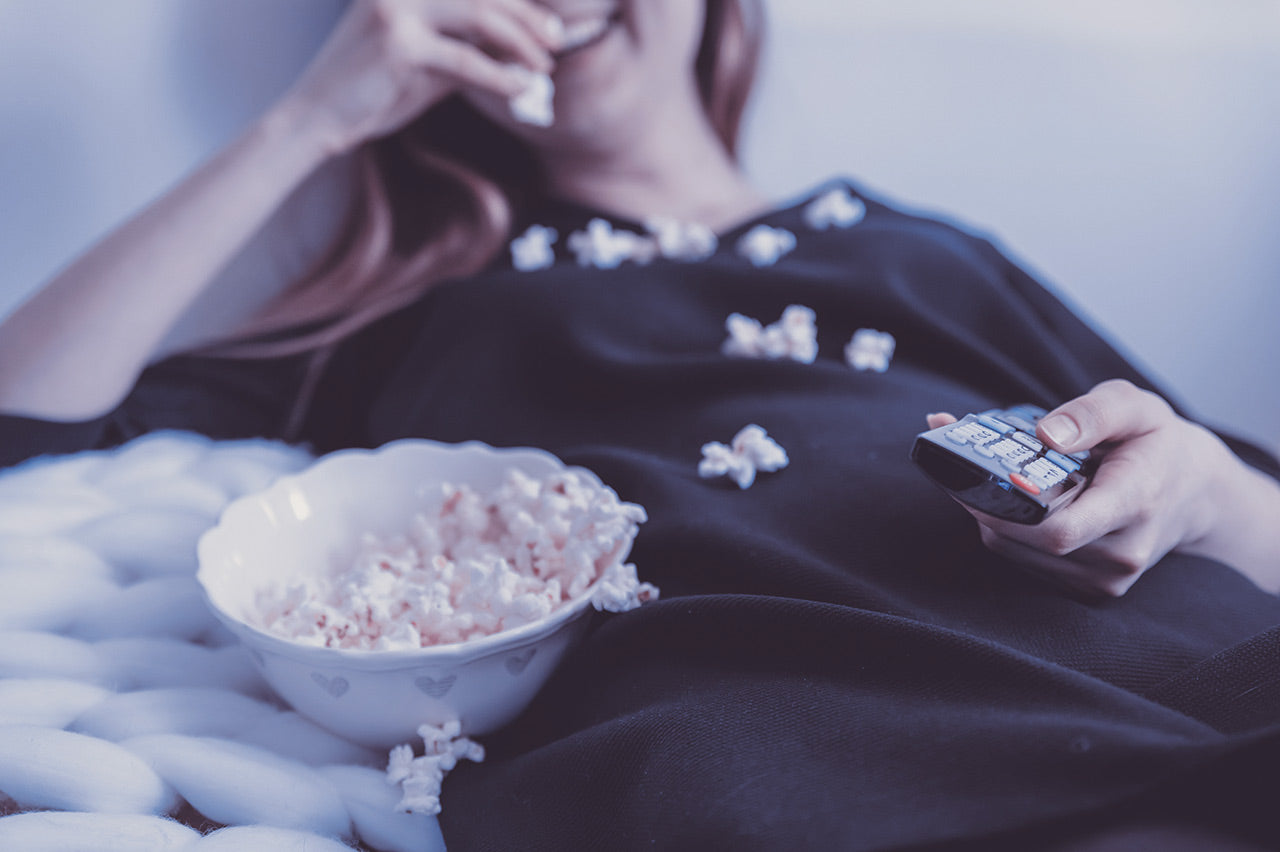 Happy woman watching TV and eats popcorn at night.