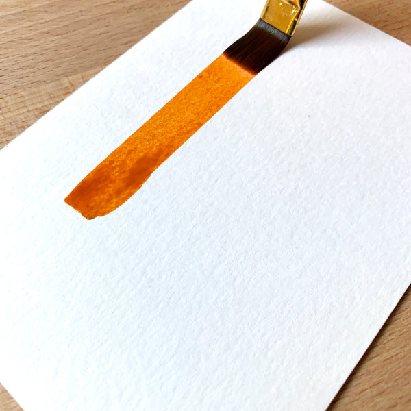 Close up of a paint brush filled with orange paint on paper