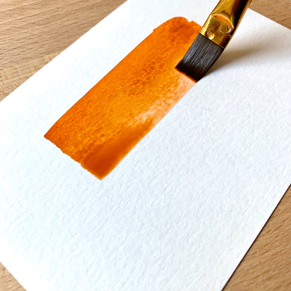 Close up of a paint brush filled with orange paint on paper