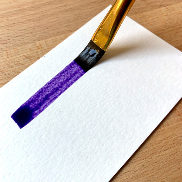 Close up of brush filled with purple paint on paper