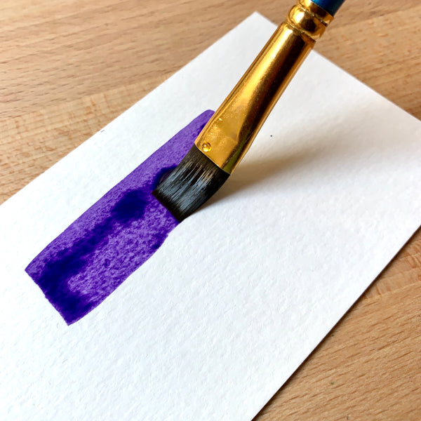 Close up of brush filled with purple paint on paper