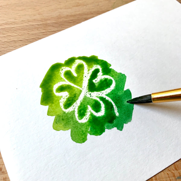 Close up of a white shamrock and some green paint on watercolour paper