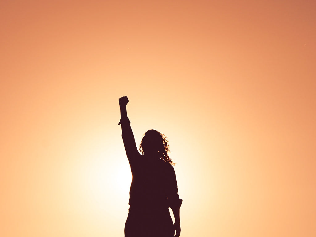 black silhouette of a woman with her hand raised in a fist with an orange background 