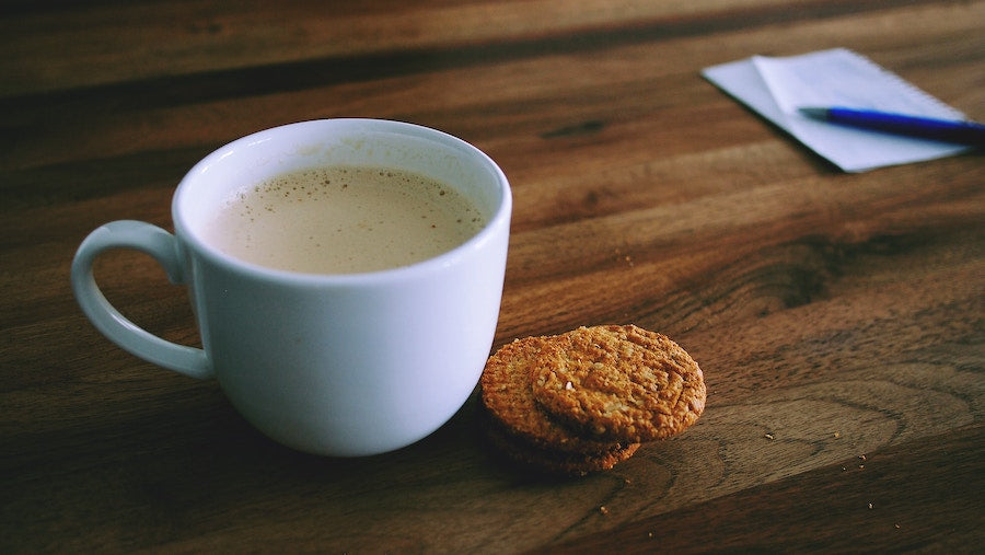 Close up image of a cappuccino and two cookies on a wooden desk
