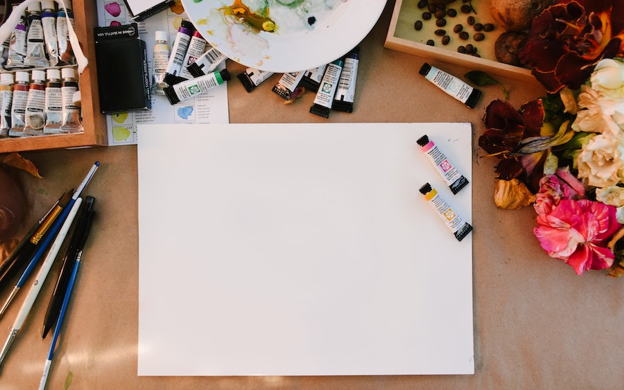 flatlay image of a white piece of paper surrounded by brushes and watercolour paints
