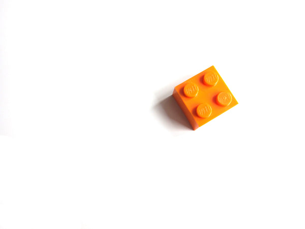 Single square orange megablock piece on the right hand side of a white background