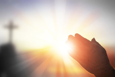 Hand praying in front of the sun 
